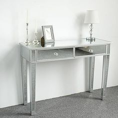 a silver mirrored desk with two drawers and a lamp on the table next to it