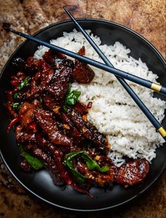 rice and meat with chopsticks in a black plate on a wooden table top