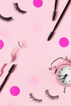 an alarm clock, eyeliners and mascara on a pink background with polka dots