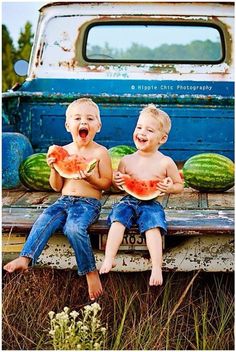 two young boys sitting on the back of a truck eating watermelon