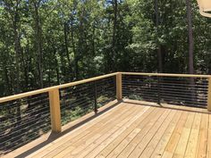 a wooden deck with metal railing and trees in the background