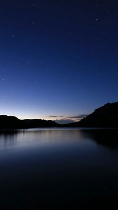 the night sky is lit up over a lake with mountains in the distance and stars above it