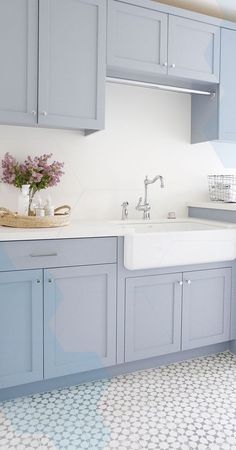 a kitchen with blue cabinets and a white sink in the center is decorated with purple flowers