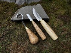 two knives are sitting next to each other on the grass near a rock and knife sharpener