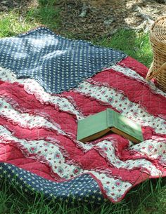 an american flag quilt with a book on it in the grass next to a wicker basket