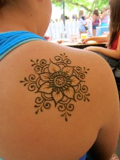 the back of a woman's shoulder with a tattoo design on her left arm