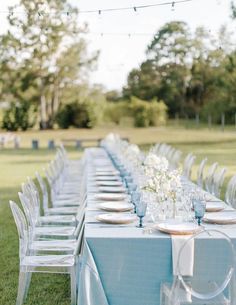 a long table is set up with clear chairs and place settings for an outdoor dinner