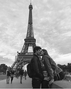 a man and woman kissing in front of the eiffel tower on a cloudy day