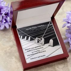 an open box with a necklace in it on a table next to flowers and purple flowers