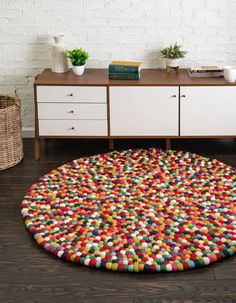 a multicolored round rug on the floor in front of a white brick wall