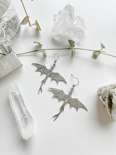 the earrings are made from metal and have bats hanging from them, along with crystals