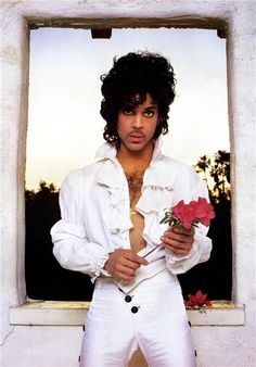 a man in white is holding a rose and posing for the camera with his shirt open