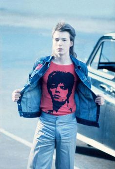 a young man is standing next to an old car wearing a jean jacket and t - shirt