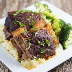 a white plate topped with meat and broccoli on top of a wooden table