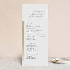 a white and gold wedding ceremony program on a marble table next to a small plate