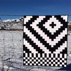 a black and white quilt hanging on a wire fence in the snow with mountains in the background