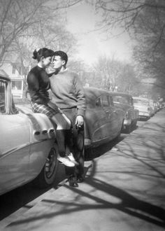 two people standing next to an old car