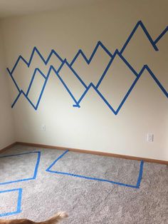 an empty room with blue tape on the wall and a dog running in front of it