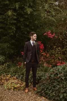 a man in a suit and tie standing next to some bushes with red flowers on it