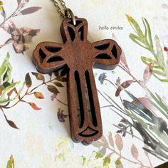 a wooden cross on a chain sitting on top of a flowered tablecloth with leaves