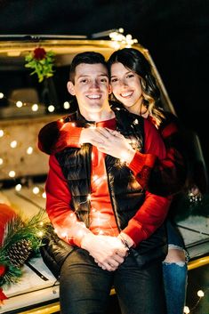 a man and woman sitting on the back of a pick up truck with christmas lights