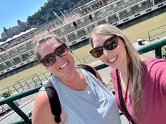 two women taking a selfie in front of a river with a cruise ship in the background