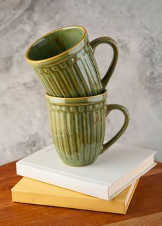 two green mugs stacked on top of each other next to some yellow and white books