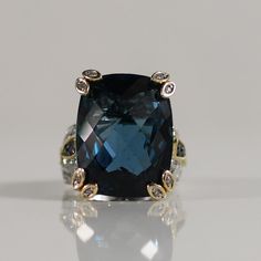 This breathtaking statement ring features an approximately 40-carat blue topaz, radiating a captivating azure hue. The striking gemstone is set in 14k white gold, secured by 14k yellow gold prongs that add a touch of warmth and contrast. Sapphire and diamond accents enhance the ring's elegance, with intricate yellow gold detailing further elevating its luxurious appeal. This piece is a true showstopper, blending boldness with refined sophistication. Size: 7 Metal Type: 14K Yellow and White Gold(Tested) Weight: 16.5G Width: 21.93mm-11.07mm at shank Finger to Top of Ring: 14.65mm Gem Details:  Type: Blue Topaz Quantity:1 Cut: Elongated Cushion w Checkerboard Top Carat: Aprox 40 carats Accent Gems: Type: Sapphire & Diamond Quantity: 20 Shape: Round Brilliant Carat Weight: aprox 0.36ctw   We l Luxury Topaz Ring With Diamond Accents And Cubic Zirconia, Luxury Fine Jewelry Topaz Ring For Formal Occasions, Exquisite Luxury Topaz Ring For Gift, Luxury Timeless Topaz Ring Gift, Luxury Modern Topaz Ring With Accent Stones, Luxury Faceted Topaz Ring For Formal Occasions, Luxury Unique Topaz Ring As Gift, Luxury Fine Jewelry Topaz Ring For Formal Events, Elegant Luxury Large Stone Topaz Ring