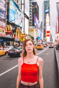 a woman standing in the middle of a city street wearing a red crop top and plaid pants