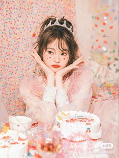 a woman sitting at a table with a cake in front of her and confetti on the wall behind her