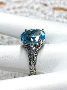 Natural Blue Topaz Sterling Silver RingMedieval Floral Design#D173 Introducing the D173 Medieval Floral ring! A gorgeous antique reproduction crafted to resemble its classic predecessors, while still boasting a modern touch. This enchanting piece of jewelry features an oval faceted gemstone, which has been prong set over stunning filigree, complete with intertwined floral designs and vine imagery that dance down the sides of the band. Thanks to this subtle balance of influences from both Art Dec Antique Oval Topaz Jewelry, Antique Oval Topaz Ring With Filigree, Heirloom Oval Topaz Ring With Intricate Design, Classic Oval Blue Topaz Filigree Ring, Oval Blue Topaz Filigree Ring With Intricate Design, Ornate Blue Oval Jewelry, Victorian Blue Oval Topaz Ring, Victorian Oval Topaz Jewelry, Turquoise Oval Topaz Ring