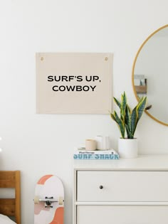 a bedroom with a skateboard and mirror on the wall next to it, along with a sign that says surf's up cowboy