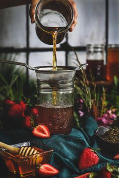 someone pouring syrup into a jar filled with strawberries