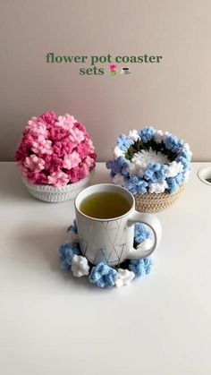 two cups filled with green tea next to pink and blue flowers on a white table