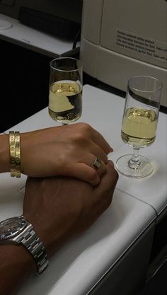 two people holding hands on an airplane table with glasses of wine in front of them