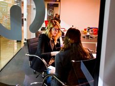 two women sitting at a table in front of a glass wall talking to each other