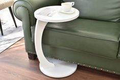 a green leather chair with a white table on the side and a coffee cup sitting on top of it