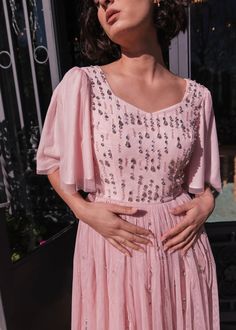 a woman in a pink dress standing next to a window with her hands on her hips