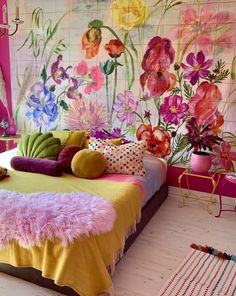 a bedroom decorated in pink, yellow and green with flowers painted on the wall behind the bed