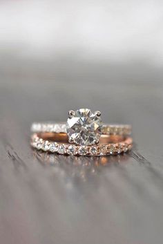 two gold wedding bands with a diamond ring on top of each other, sitting on a wooden surface