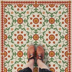 a person standing in front of a colorful rug with flowers and leaves on the floor