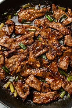 meat and vegetables cooking in a skillet on the stove top, with sauce over it