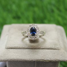 a blue and white diamond ring sitting on top of a velvet box with grass in the background