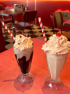 two drinks with whipped cream and chocolate are sitting on a red table in a restaurant