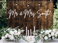 a table topped with white flowers and candles next to a wooden sign that says mr and mrs smith