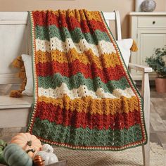 a crocheted blanket sitting on top of a white chair next to a potted plant