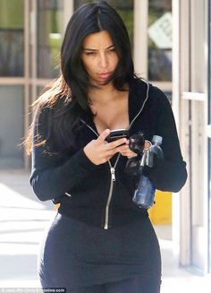 a woman in tight black clothing is looking at her cell phone and holding a camera