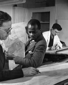 two men are looking at a map while another man is writing something on the table