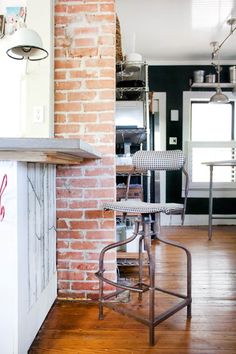 a brick wall in a kitchen with an old fashioned bar stool next to the stove