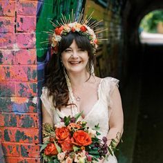 a woman holding a bouquet in front of a brick wall with graffiti painted on it